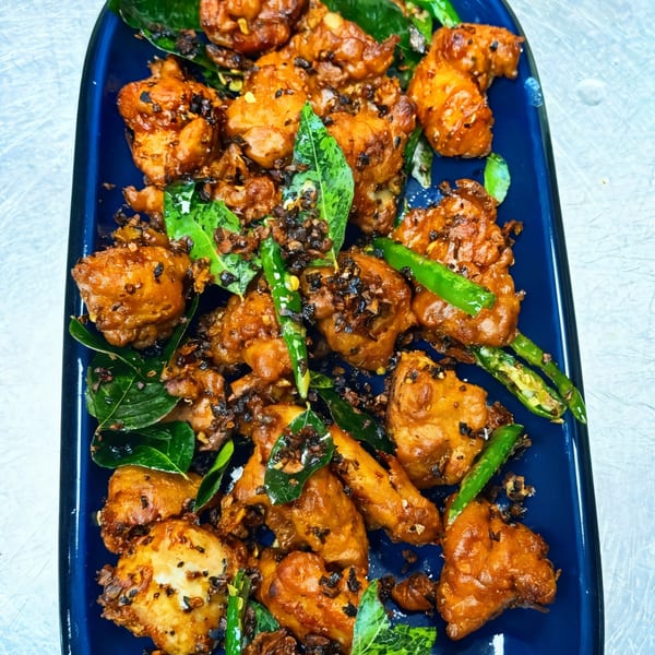 Indian fried chicken pieces with green chilies and curry leaves on a blue platter.