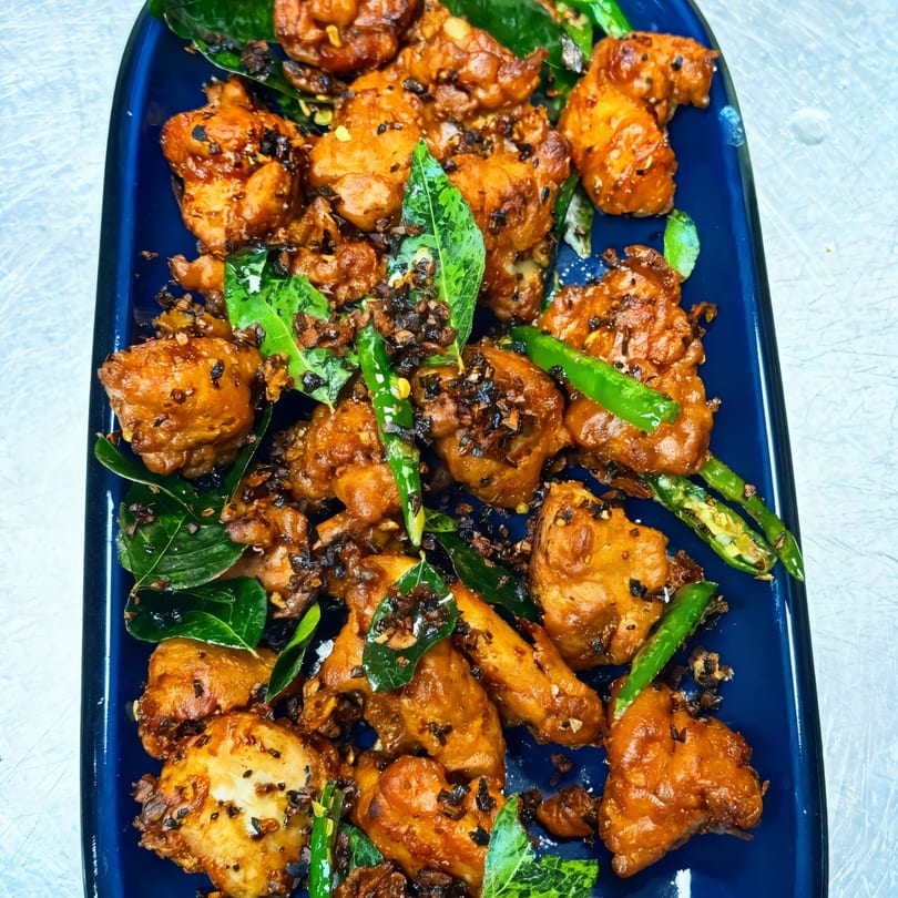 Indian fried chicken pieces with green chilies and curry leaves on a blue platter.