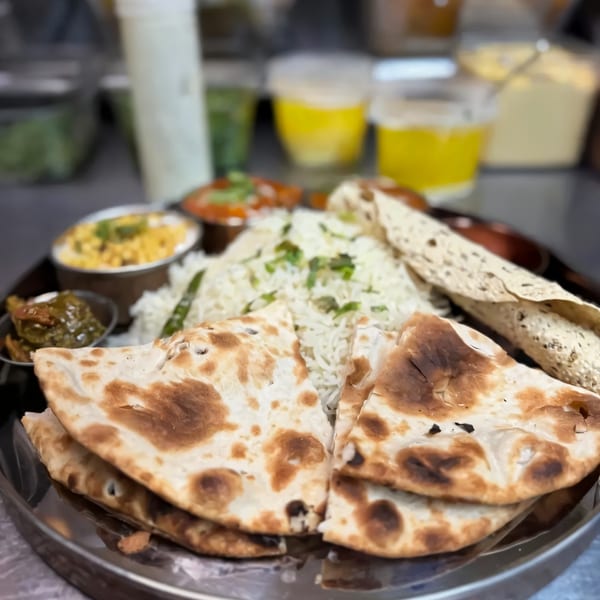 A Charcoal Eats Katy Indian thali with naan, rice, dal, curry, and papadum on a metal plate.