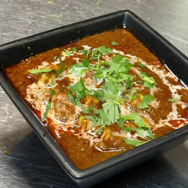 Indian curry with cream swirls and fresh cilantro in a black square bowl.
